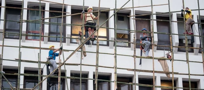 Stavební dělníci pracují na lešení u budovy.