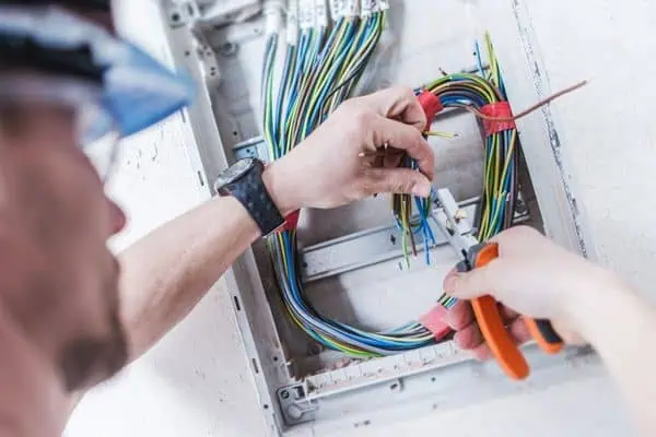 Elektrikář zapojuje vodiče v rozvaděči pomocí kleští.