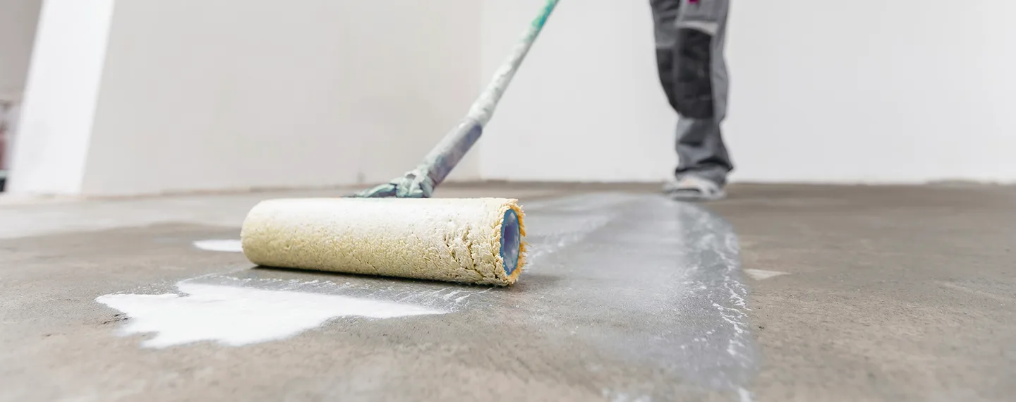 Průvodce hloubkovou penetrací: aplikátor rozšiřuje bílou impregnaci na betonovou podlahu.
