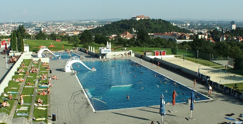 Venkovní bazén na kopci s tobogány a lehátky.