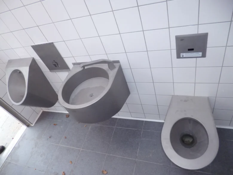 Moderní veřejná toaleta s umyvadly a záchody na bílých dlaždicích.