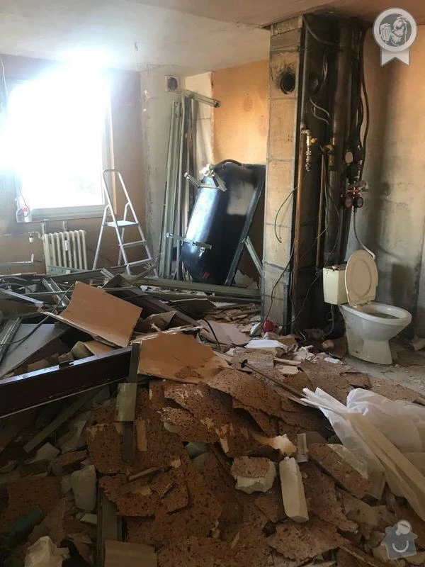 Zničená koupelna po demolici s rozbitými dlažbami a odhaleným potrubím.
