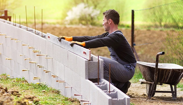 Muž staví betonový plot s použitím ztraceného bednění a výztuže.