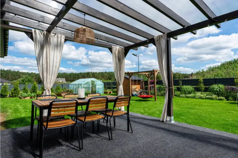 Pergola s plastovou střechou na zahradě s jídelním stolem.