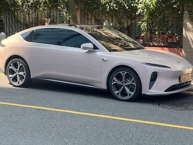 Bílé elektromobil zaparkovaný na ulici s stromy v pozadí.