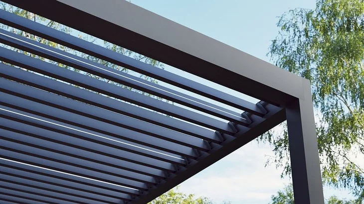 Moderní tmavá bioklimatická pergola s lamelami na pozadí modré oblohy.