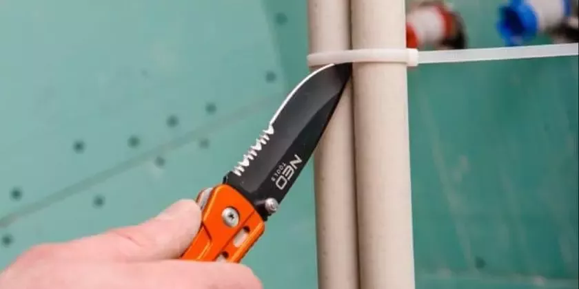 Ruka drží nůž pro řezání plastového svorky na potrubí.