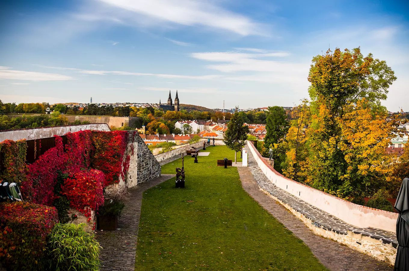 Zpevněná zahrada s červenou révou a výhledem na město.