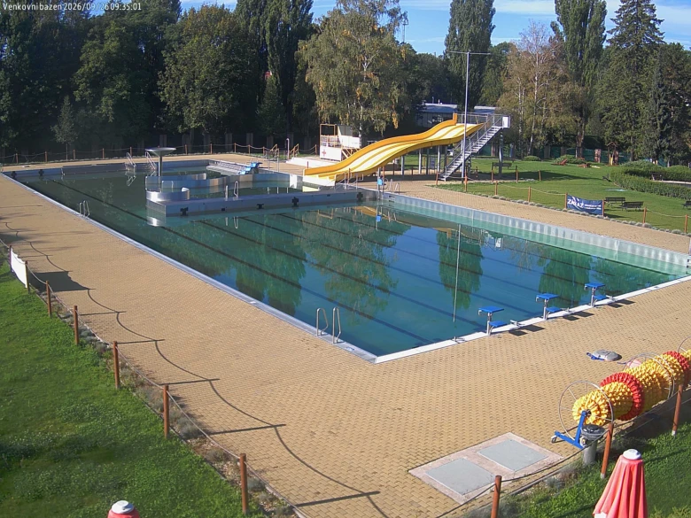 Venkovní bazén s žlutou vodní skluzavkou v parku.