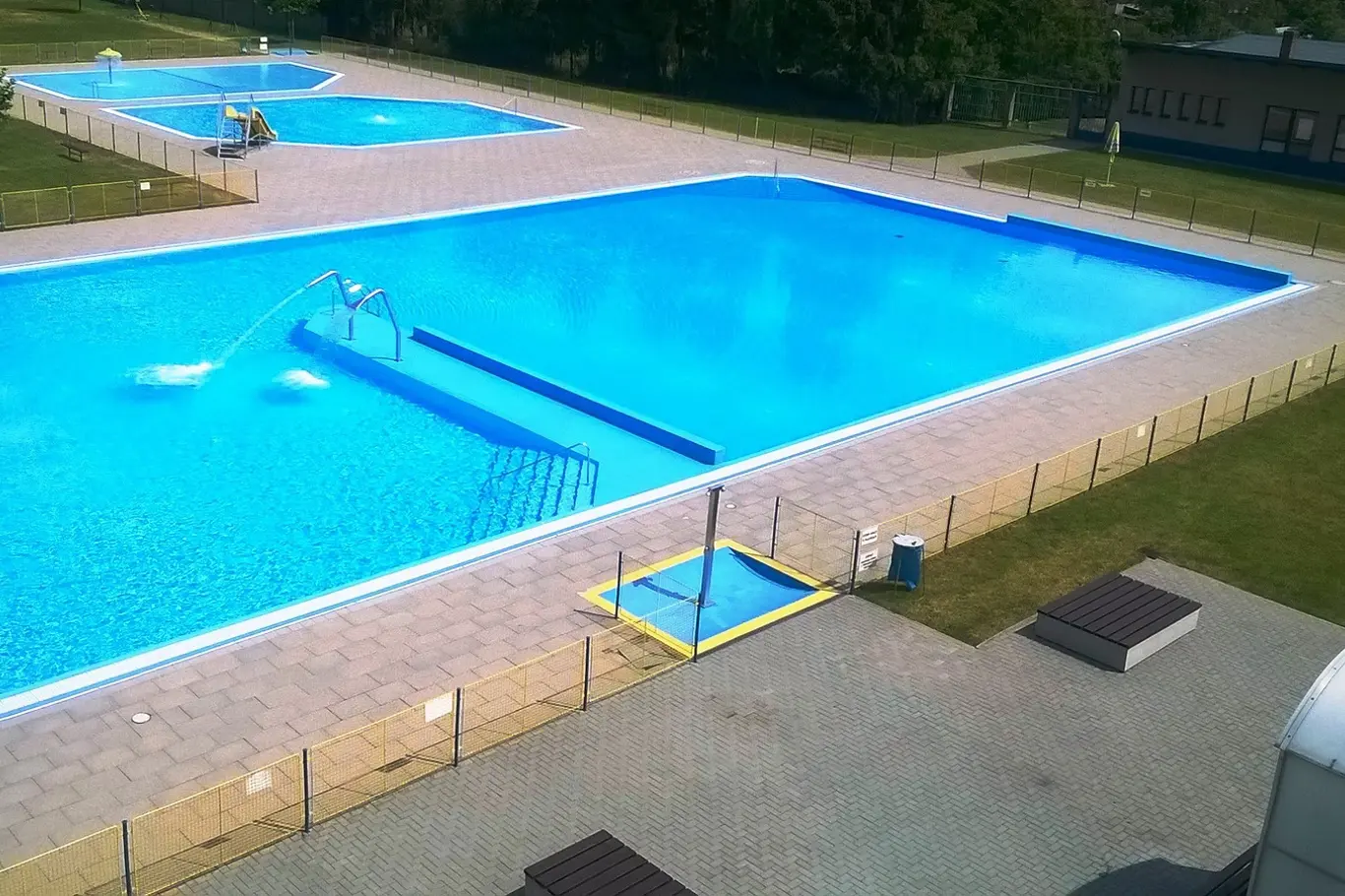 Více bazénů v areálu venkovního koupaliště s přírodní osvětlením.
