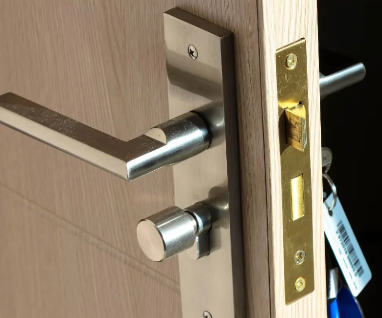 Detail zámku dveří s klikou na hraně dřevěné desky.
