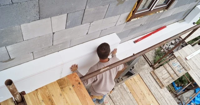 Muž lepi bílý polystyren na šedou cihlovou zeď.