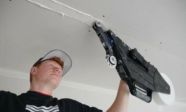 Muž nanáší tmel na spoji sádrokartonu stropu pomocí nástroje.