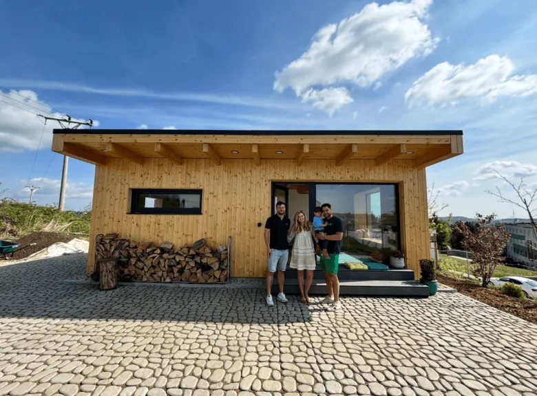 Rodina stojí před dřevěným tiny housem na kamenné ploše.