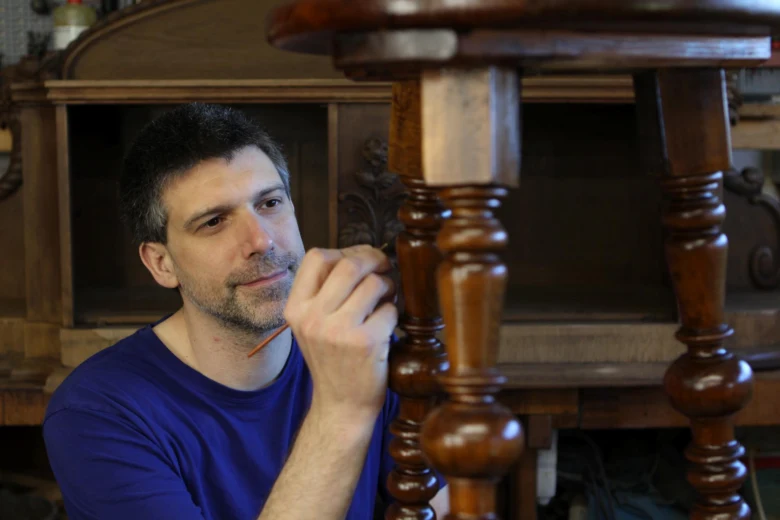 Muž restařuje starý dřevěný nábytek malováním nohy stolu.