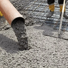 Zelený beton se nalévá na ocelovou výztuž s pracovníky v pozadí.