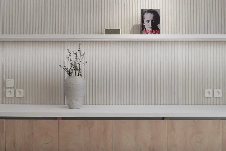 Moderní interiér s vertikálními panely za bílou pracovní deskou.
