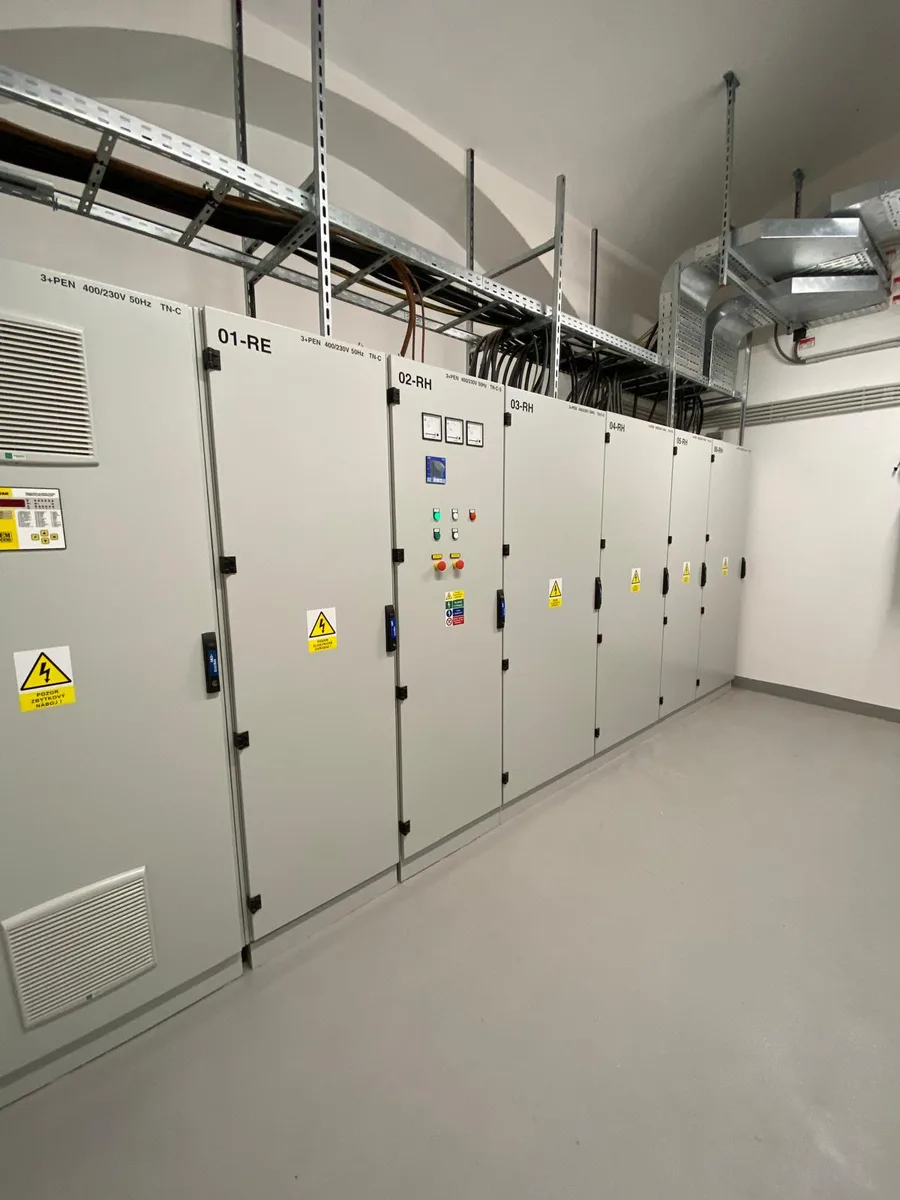 Řada průmyslových elektrických rozváděčů v čistém prostoru s kabelovými drážkami.
