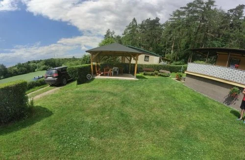 Dřevěná zahradní pergola s posezením na trávníku.