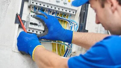 Elektrikář opravuje rozvaděč s viditelným zapojením kabelů.