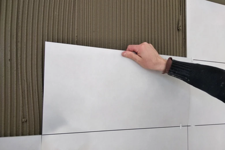 Ruka položí velkoformátovou dlažbu na stěnu s lepidlem.