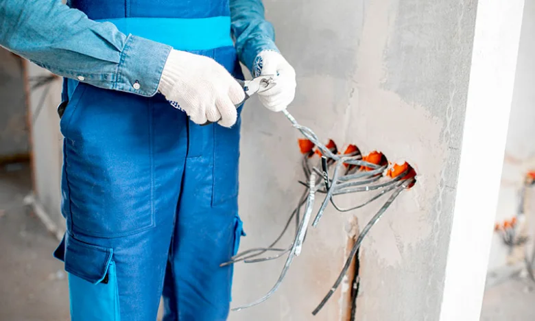 Elektrikář upravuje dráty v zdi při instalaci zásuvek.