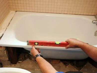Pracovník kontroluje úroveň okraje staré smaltované vany při renovaci.