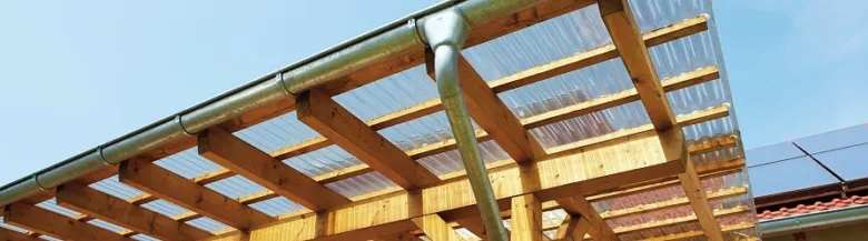 Pergola s plastovou střešní krytinou na pozadí modré oblohy.