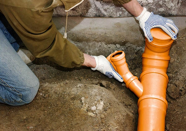 Instalace oranžových odpadních kanalizačních trubek do výkopu.