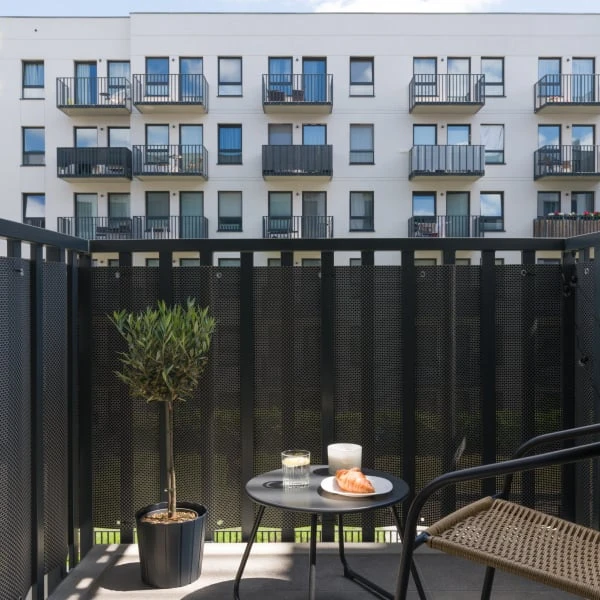 Malý balkon v paneláku s rostlinou, stolkem a židlí.