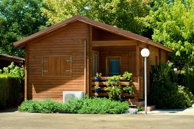 Dřevěný zahradní domek s okny a kvetoucími rostlinami.