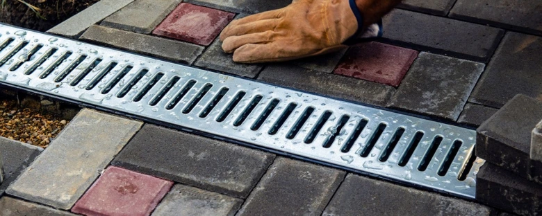 Instalace odtokového žlabu do dlažby v zahradě s rukavicí.