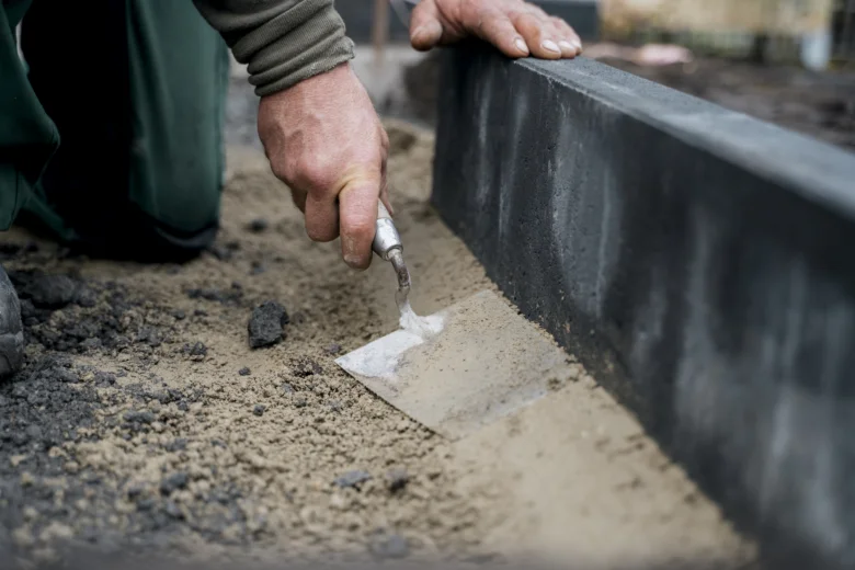 Muž pokládá obrubník pomocí malého špachtle na betonu.