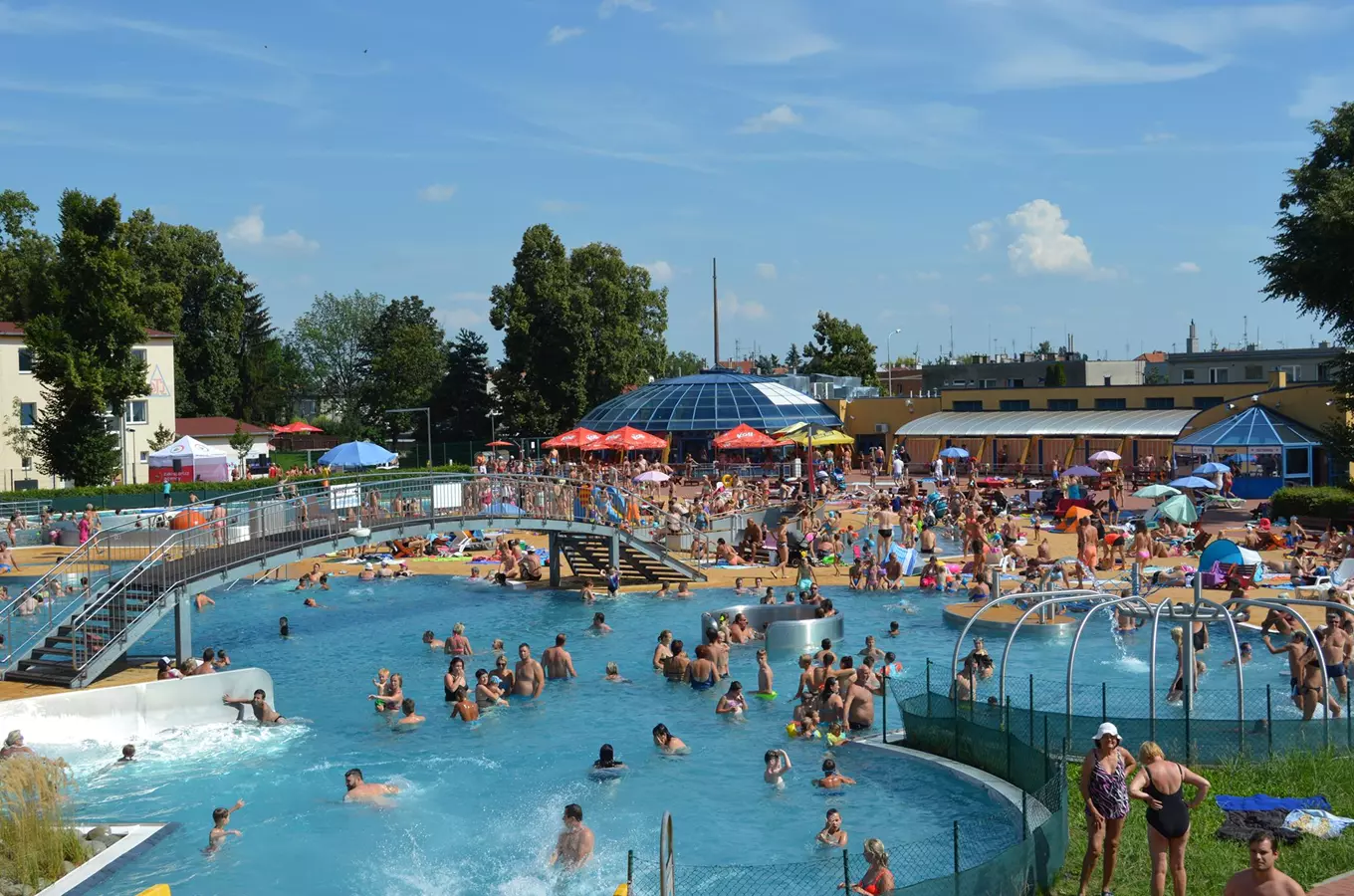 Lidé plavou v bazénu na koupališti s aquaparkem.