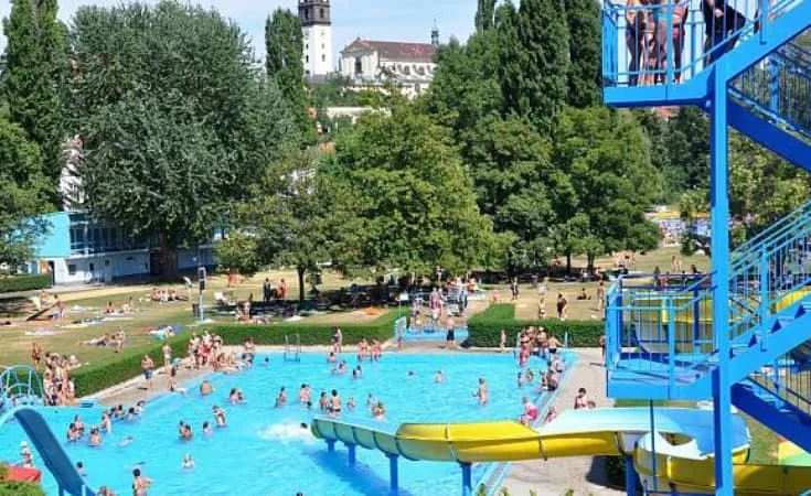 Venkovní plavecký bazén s vodními skluzavkami a lidmi koupející se v Praze nebo okolí.