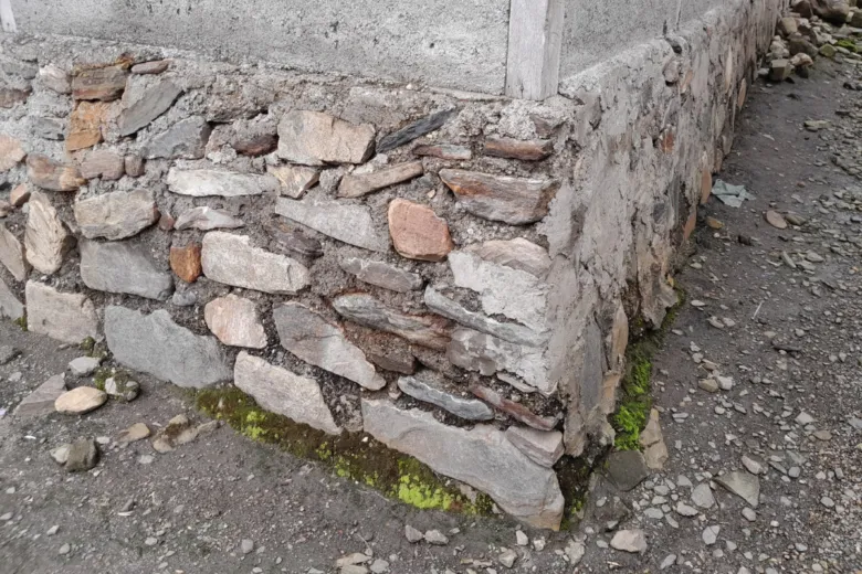 Kout starého kamenného základu domu s viditelnou hydroizolací.