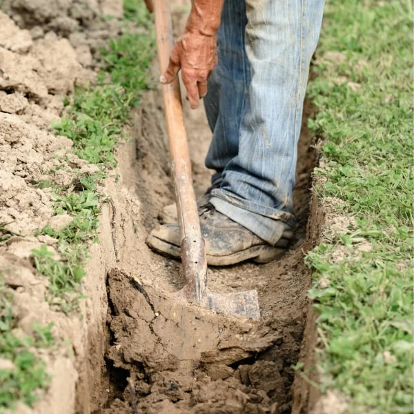 Člověk kopá příkop pro drenážní systém zahradou.