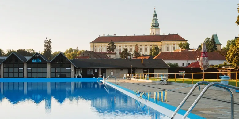 Venkovní bazén v Bajdě s historickým klášterem na pozadí.