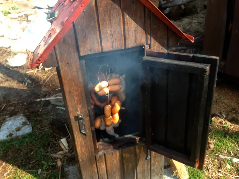 Dřevěná udírna svépomocí s uzenými klobásami a kouřem venku.