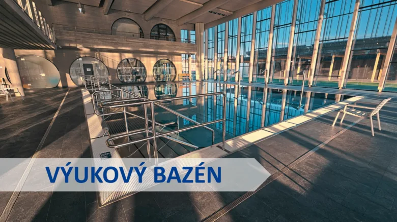 Vnitřní plavecký bazén s velkými okny a kovovými zábradlím.
