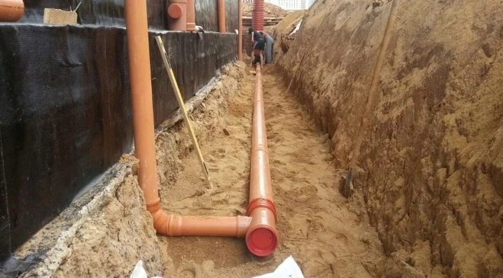 Instalace oranžové odvodňovací trubice do příkopu u domu.