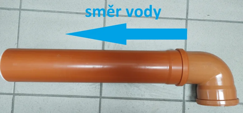 Oranžová plastová ohybová spojka pro odpadní systém s šipkou směr vody.