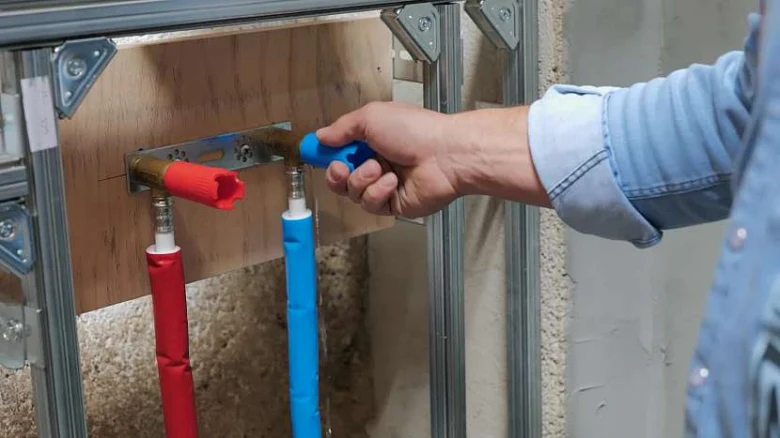 Ruka provádí tlakovou zkoušku vodovodního potrubí v instalační skříni.