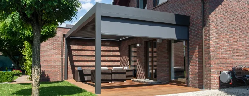 Moderní hliníková pergola na dřevěné terase u cihlového domu.