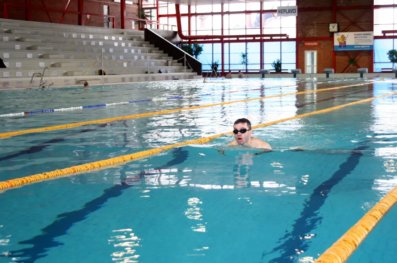 Muž plave na zádech v krytém bazénu s dálnicemi.
