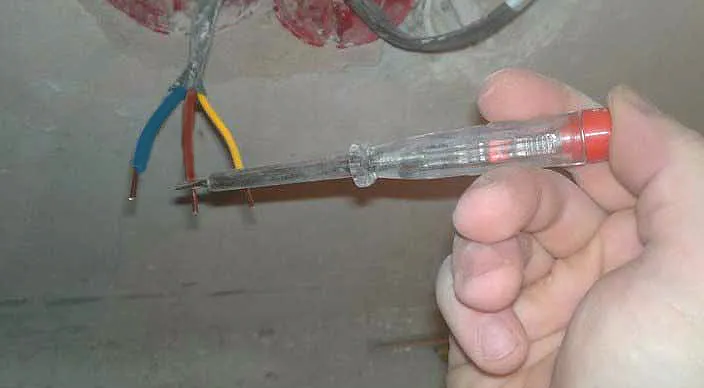 Ruka drží testovací šroubovák u odhalených elektrických vodičů.