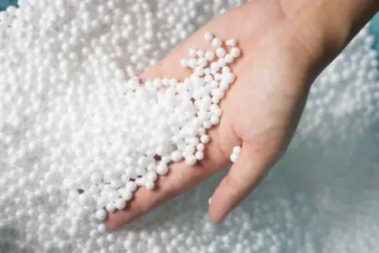 Ruka drží bílé zrnka expandovaného polystyrenu pro izolaci.