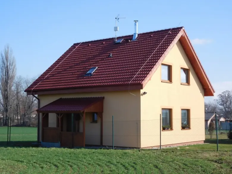 Dřevostavba s červenou střechou na zelené louce.