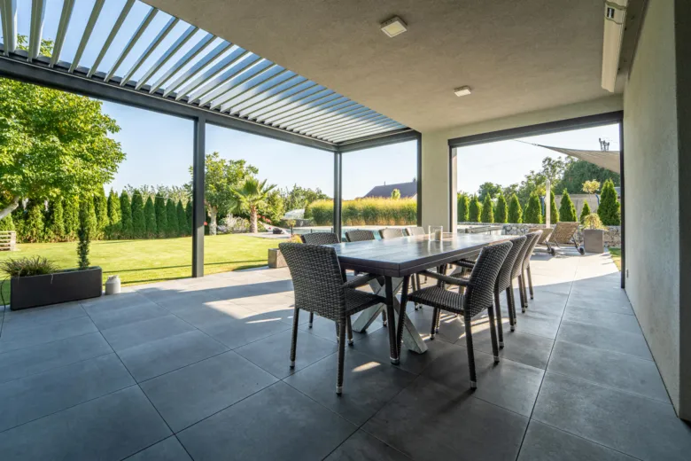 Moderní bioklimatická pergola s jídelním stolem na zahradě.