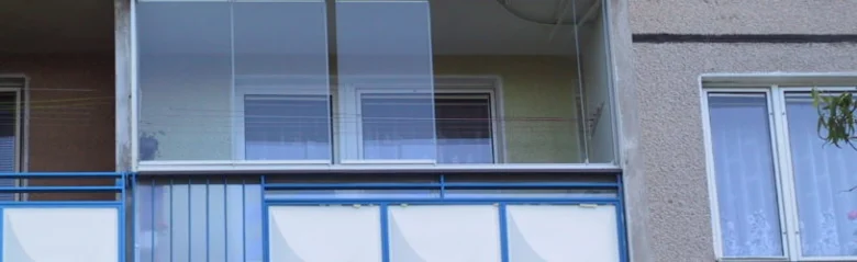 Zasklený balkon s průhlednými skelnými panely a modrým zábradlím.